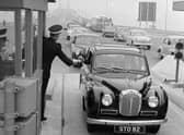 A driver pays the toll at the Forth Road Bridge in 1964, handing the money to a uniformed collector ... and how cars have changed too!
