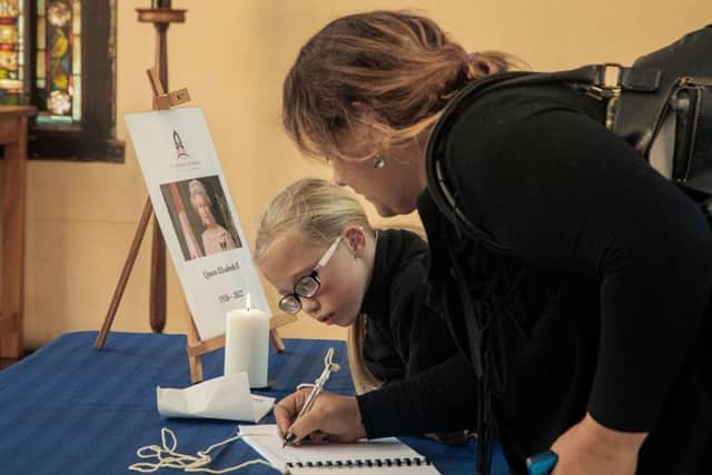 A candle burns by a portrait of the late Queen Elizabeth II as a woman signs a guest book marking her passing at the entrance of St George cathedral in Cape Town, South Africa.