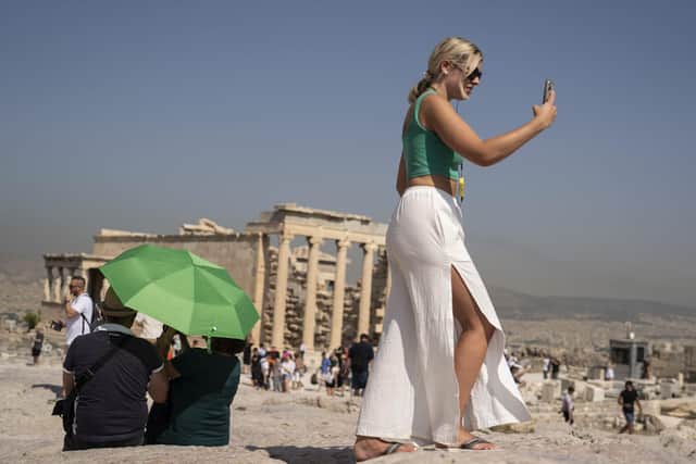 A tourist takes a selfie as a couple sit under an umbrella in front of the five century BC Erechteion temple at the Acropolis hill during a heatwave, in Athens, Greece. Picture: AP Photo/Petros Giannakouris