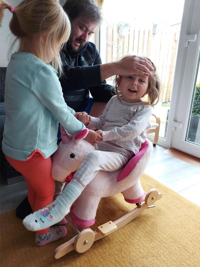 Scarlett playing on her unicorn toy with dad and little sister.