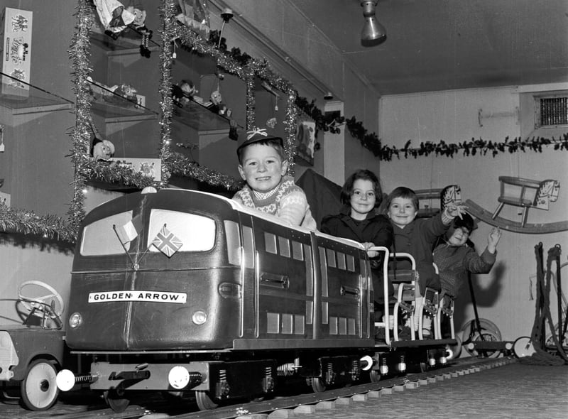 Children here are playing on a model of the Golden Arrow engine in Jenners in November - tinsel and Christmas decorations can be seen on the shelves. Year: 1965