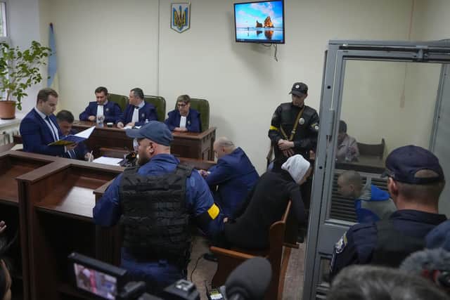 Sitting behind a glass, Russian army Sergeant Vadim Shishimarin, 21, talks with his translator, centre right, during a court hearing in Kyiv, Ukraine, Wednesday, May 18, 2022. The Russian soldier has gone on trial in Ukraine for the killing of an unarmed civilian. The case that opened in Kyiv marked the first time a member of the Russian military has been prosecuted for a war crime since Russia invaded Ukraine 11 weeks ago. (AP Photo/Efrem Lukatsky)