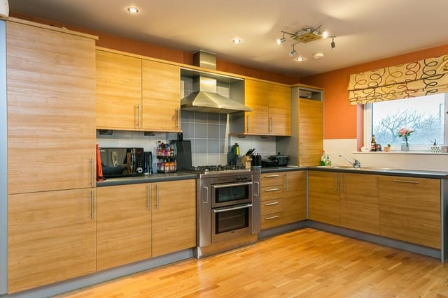 Set to one side, the modern kitchen features stone-effect worktops, sink with drainer, tiled surround, integrated dishwasher, fridge/freezer, and range-style double oven with gas hob and canopy above.