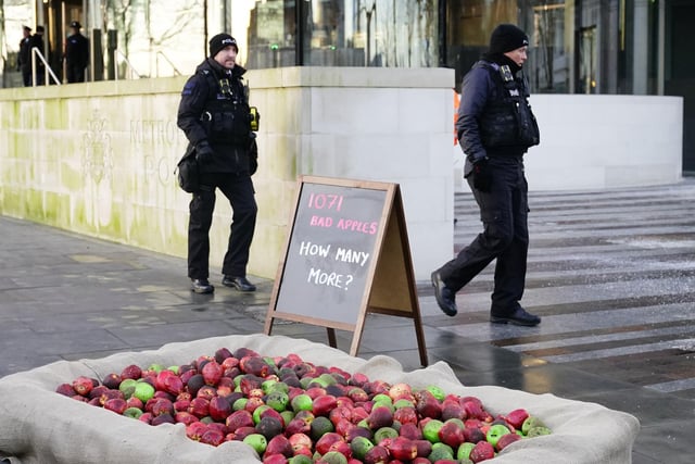 Police officers walk past 1,071 rotten apples outside New Scotland Yard