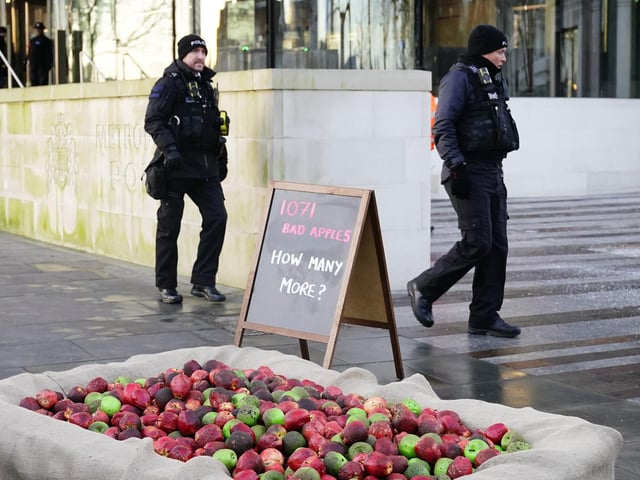 Police officers walk past 1,071 rotten apples outside New Scotland Yard