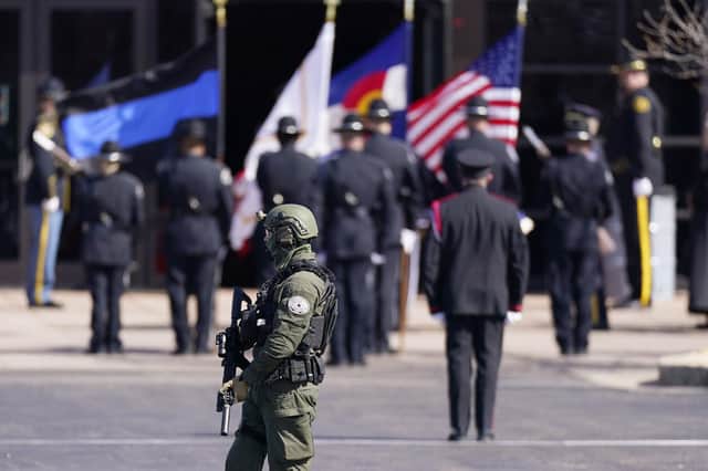 An officer in tactical gear carries a long gun while patrolling as a casket is unloaded for a memorial service for police officer Eric Talley. Talley and nine other people died in a mass shooting on Monday, March 22