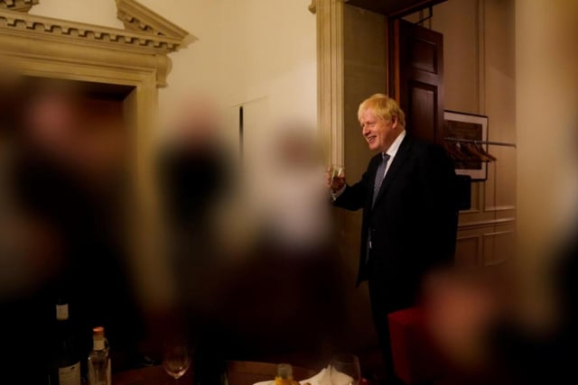 Boris Johnson smiles during the gathering, with wine bottles and glasses visible in the foreground of the image.