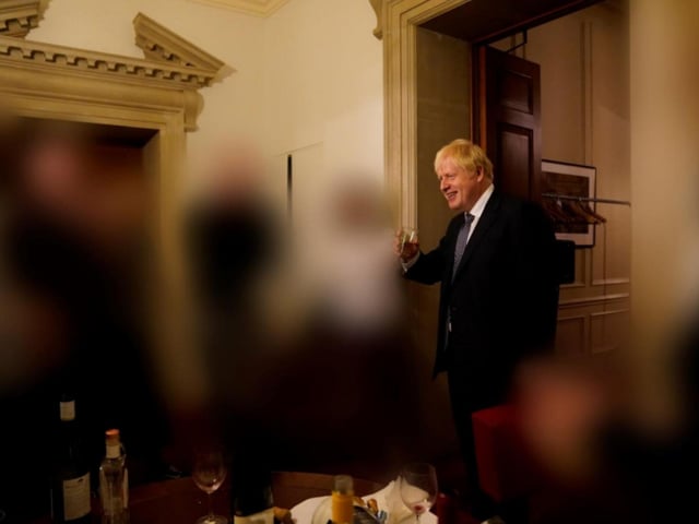 Boris Johnson smiles during the gathering, with wine bottles and glasses visible in the foreground of the image.