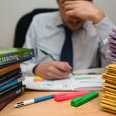 A school teacher looking stressed next to piles of classroom books. PA/PA Wire