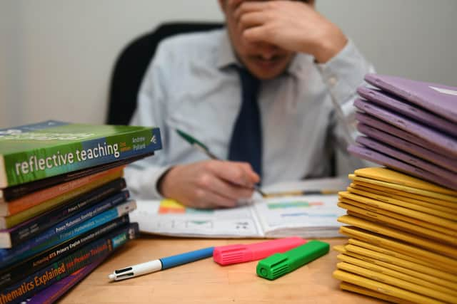 A school teacher looking stressed next to piles of classroom books. PA/PA Wire