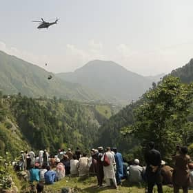People watch as an army soldier slings down from a helicopter during a rescue mission to recover students stuck in a chairlift in Pashto village of mountainous Khyber Pakhtunkhwa province, on August 22, 2023. Six children and two adults were suspended inside a cable car dangling over a deep valley in Pakistan for several hours on August 22, as a military helicopter hovered nearby. (Photo by Prateek KUMAR / AFP) (Photo by PRATEEK KUMAR/AFP via Getty Images)