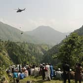 People watch as an army soldier slings down from a helicopter during a rescue mission to recover students stuck in a chairlift in Pashto village of mountainous Khyber Pakhtunkhwa province, on August 22, 2023. Six children and two adults were suspended inside a cable car dangling over a deep valley in Pakistan for several hours on August 22, as a military helicopter hovered nearby. (Photo by Prateek KUMAR / AFP) (Photo by PRATEEK KUMAR/AFP via Getty Images)