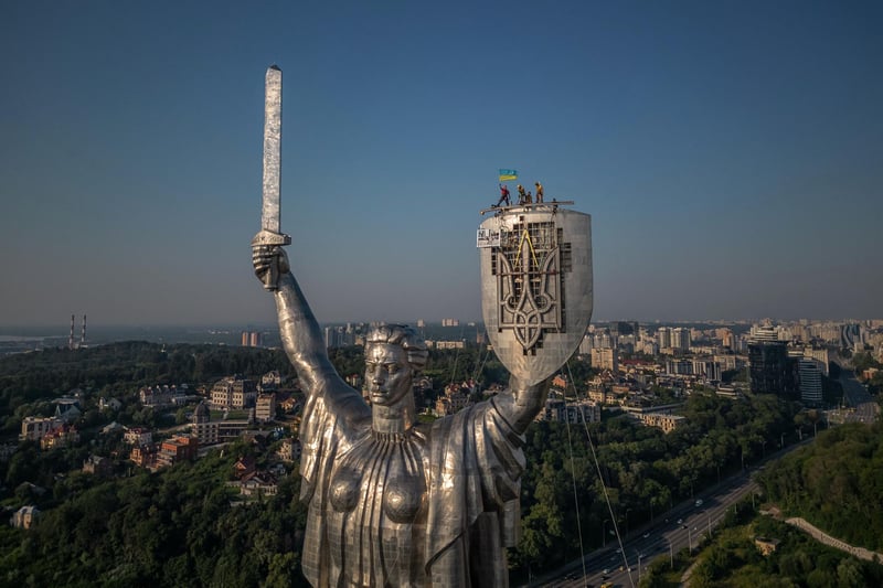 Steeplejacks wave the Ukrainian flag after finishing installing the coat of arms of Ukraine on the shield of the 62 metre Motherland Monument in Kyiv, on August 6, 2023