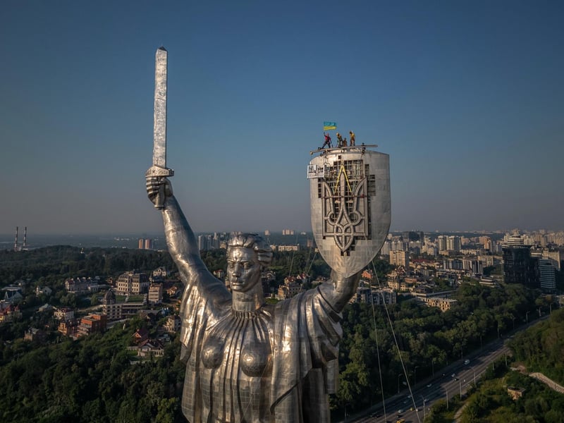 Steeplejacks wave the Ukrainian flag after finishing installing the coat of arms of Ukraine on the shield of the 62 metre Motherland Monument in Kyiv, on August 6, 2023