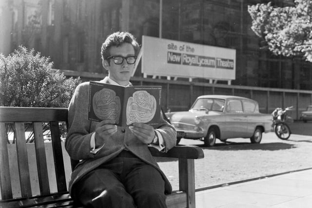 A visitor sits in Castle Terrace reading the Edinburgh International Festival guide book in August 1966. The sign behind him reads 'Site of the New Royal Lyceum Theatre'.