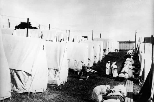 Masked doctors and nurses treat flu patients lying on cots and in outdoor tents at a hospital camp during the influenza epidemic of 1918. (Photo by Hulton Archive/Getty Images)