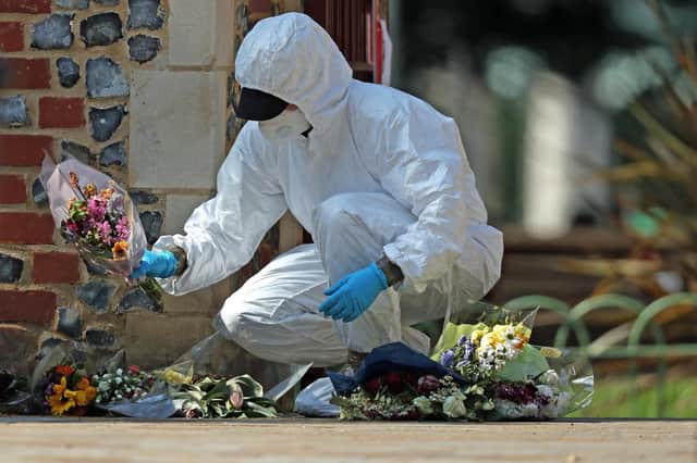A forensic officer searches floral tributes laid at Forbury Gardens, Reading, where three people were killed and three seriously injured (Picture: Steve Parsons/PA Wire)