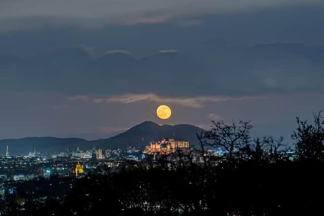 This spectacular image shows a ghostly, spectre-like  moon hanging above Edinburgh Castle