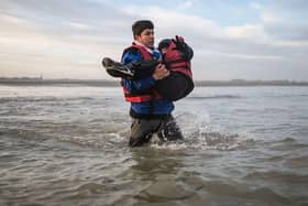 A man carries a child as he runs to board a smuggler's boat in northern France last month, in an attempt to cross the English Channel.