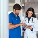 Doctor and nurse discussing over a medical report in hospital. Female mature doctor and nurse checking clinical report of patient online. Healthcare staff having discussion in a hallway of private clinic.