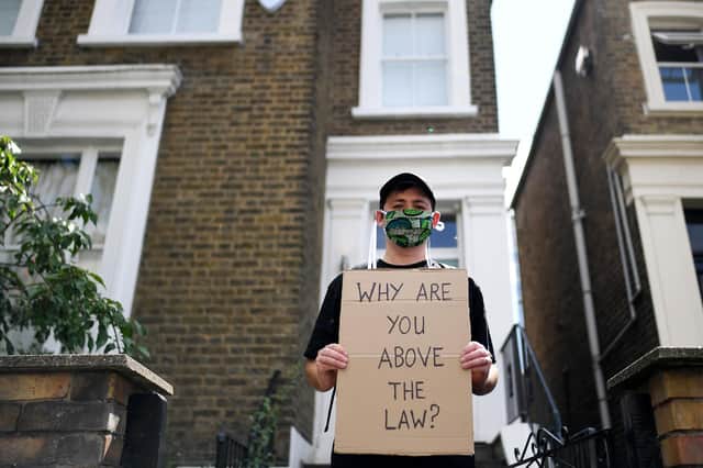 A protester holds up a placard which reads 'Why are you above the law?' outside the home of Dominic Cummings