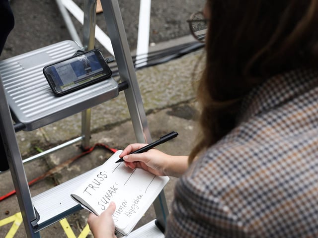 A journalist writes down the results of the election of the new the new Conservative party leader and Britain's Prime Minister as she watches the results on a live streeam on her phone form Downing Street in central London on September 5, 2022, the final full day of Boris Johnson's Premiership