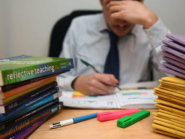 A school teacher looking stressed next to piles of classroom books. PA/PA Wire