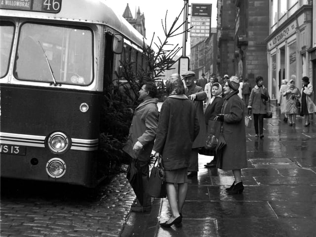 A man with a Christmas tree trying to get on a bus on the High Street in Edinburgh