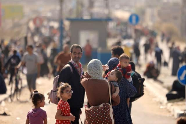 A Palestinian woman gives water to her child as families fleeing Gaza City and other parts of northern Gaza towards the southern areas, walk along a main road.