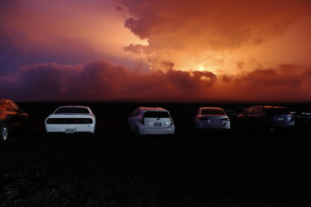 Car are parked near an ancient lava field as a lava flow colors the sky above Mauna Loa, Monday, Nov. 28, 2022, near Hilo, Hawaii. Mauna Loa, the world's largest active volcano erupted Monday for the first time in 38 years. (AP Photo/Marco Garcia)