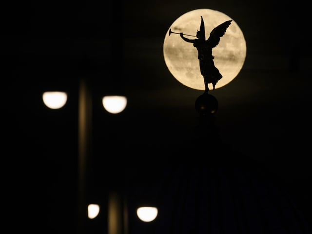 The full moon rises in the evening behind the angel "Fama" on the the Academy of Fine Arts, Tuesday, June 14, 2022, in Desden, Germany. (Robert Michael/dpa via AP)
