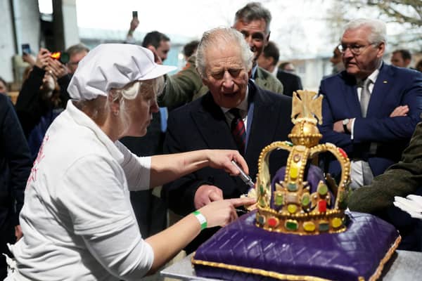 King Charles is helped by an employee to cut a cake in the shape of a crown during his state visit to Germany last month (Picture: Jens Büttner/pool/AFP via Getty Images)