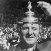 The Doc tips his makeshift hat - the FA Cup final lid - to his exciting Manchester United team after their 1977 Wembley triumph.