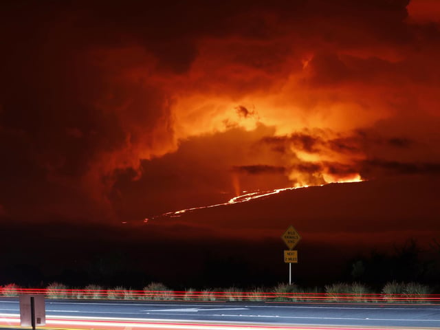 In this long camera exposure, cars drive down Saddle Road as Mauna Loa erupts in the distance, Monday, Nov. 28, 2022, near Hilo, Hawaii. Mauna Loa, the world's largest active volcano erupted Monday for the first time in 38 years. (AP Photo/Marco Garcia)