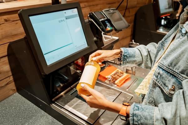 A customer scans and pays for a bottle of juice from a supermarket at an automated self-service checkout terminal. PIC: Adobe