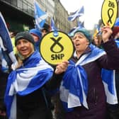 Pro-independence protesters hold up Scottish National Party (SNP) emblems as they join a march organised by the grassroots organistaion All Under One Banner