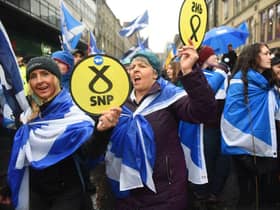 Pro-independence protesters hold up Scottish National Party (SNP) emblems as they join a march organised by the grassroots organistaion All Under One Banner
