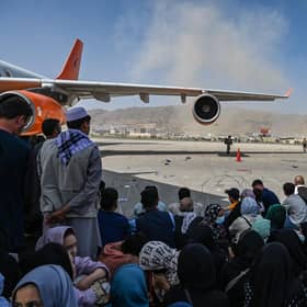 People sit on the tarmac as they wait to leave the Kabul airport on Monday following the Taliban's takeover of the city (Picture: Wakil Kohsar/AFP via Getty Images)