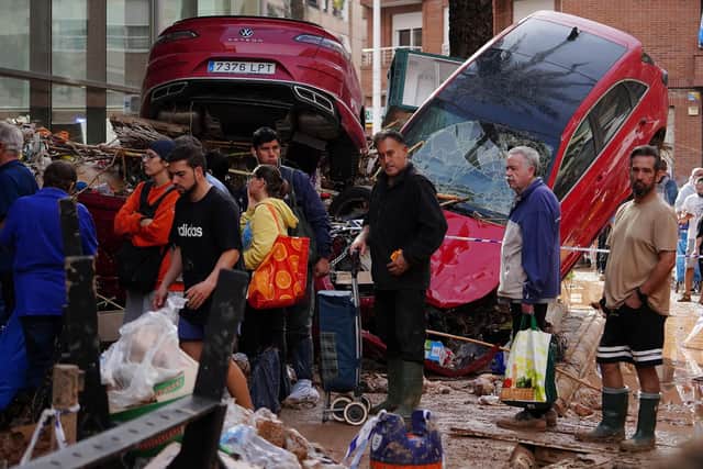 People queue for supplies close to a pile of wrecked cars following the devastating effects of flooding on the town of Paiporta, in the region of Valencia (Picture Manuare Quintero/AFP via Getty Images)