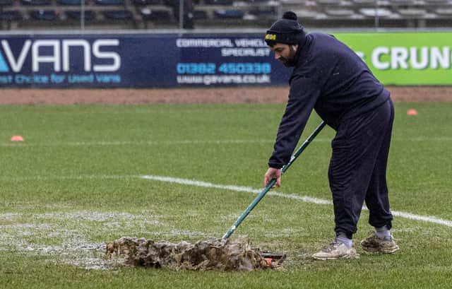 A Dundee groundsman sweeps water off the pitch at Dens Park prior to the match against Aberdeen being postponed. (Photo by Mark Scates / SNS Group)