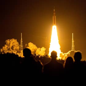 Spectators watch as the Artemis I unmanned lunar rocket lifts off from launch pad