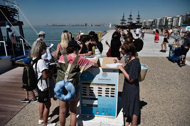 Tourists wear protective face masks as they fill in a form for before embarking on as small cruise boat along the waterfront of the northern city Greek of Thessaloniki. (Photo by SAKIS MITROLIDIS/AFP via Getty Images)