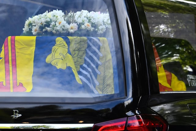 The hearse carrying the coffin of Queen Elizabeth II covered with the Royal Standard of Scotland and flowers is driven away from Balmoral Castle (Photo by ANDY BUCHANAN/AFP via Getty Images)