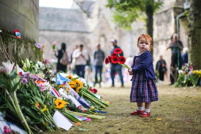 A young girl is seen laying flowers in remembrance of the late Queen Elizabeth II outside the Palace of Holyroodhouse on September 12, 2022. (Photo by Peter Summers/Getty Images)
