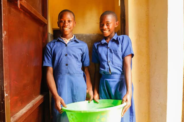 Lucie, 13, and Diane, 12, standing with a bucket in the doorway of a stall in the new menstrual hygiene management room at Ecole Primaire Muyange in Nyamagabe District, Rwanda, in February last year (Picture: WaterAid/James Kiyimba)