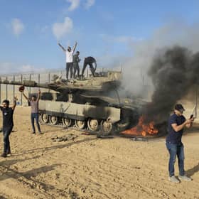 Palestinians celebrate by a destroyed Israeli tank at the Gaza Strip fence east of Khan Younis Saturday, Oct. 7, 2023. The militant Hamas rulers of the Gaza Strip carried out an unprecedented, multi-front attack on Israel at daybreak Saturday, firing thousands of rockets as dozens of Hamas fighters infiltrated the heavily fortified border in several locations by air, land, and sea and catching the country off-guard on a major holiday (AP Photo/Hassan Eslaiah)