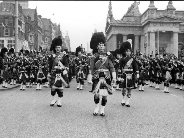 The Pipes and Drums of units performing at the Edinburgh Military Tattoo in 1964 march along Princes Street watched by a large crowd.