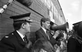 A policeman watches as Shareholders' Association chairman Ewan Stewart addresses the hundreds of angry Hibs fans who turned up at Easter Road football stadium after hearing Hearts chairman Wallace Mercer planned a takeover of their club in June 1990.