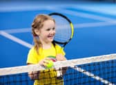 Child playing tennis on indoor court.