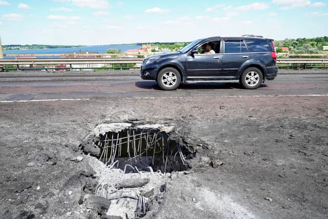 A picture taken on July 21, 2022 shows a car moving past a crater on Kherson's Antonovsky (Antonivskiy) bridge across the Dnipro river caused by a Ukrainian rocket strike, amid the ongoing Russian military action in Ukraine. (Photo by STRINGER / AFP) (Photo by STRINGER/AFP via Getty Images)